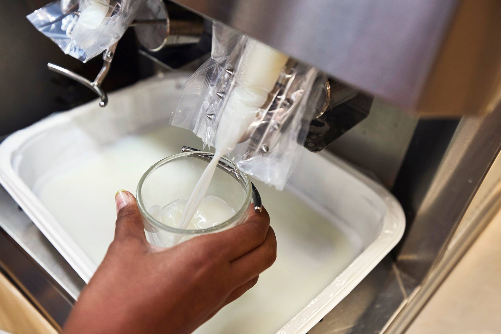 Kädessä olevalla lasilla painetaan maitoautomaatin alaosaa, ja lasiin valuu automaatista maitoa. Juomat ovat osa kouluruokaa.