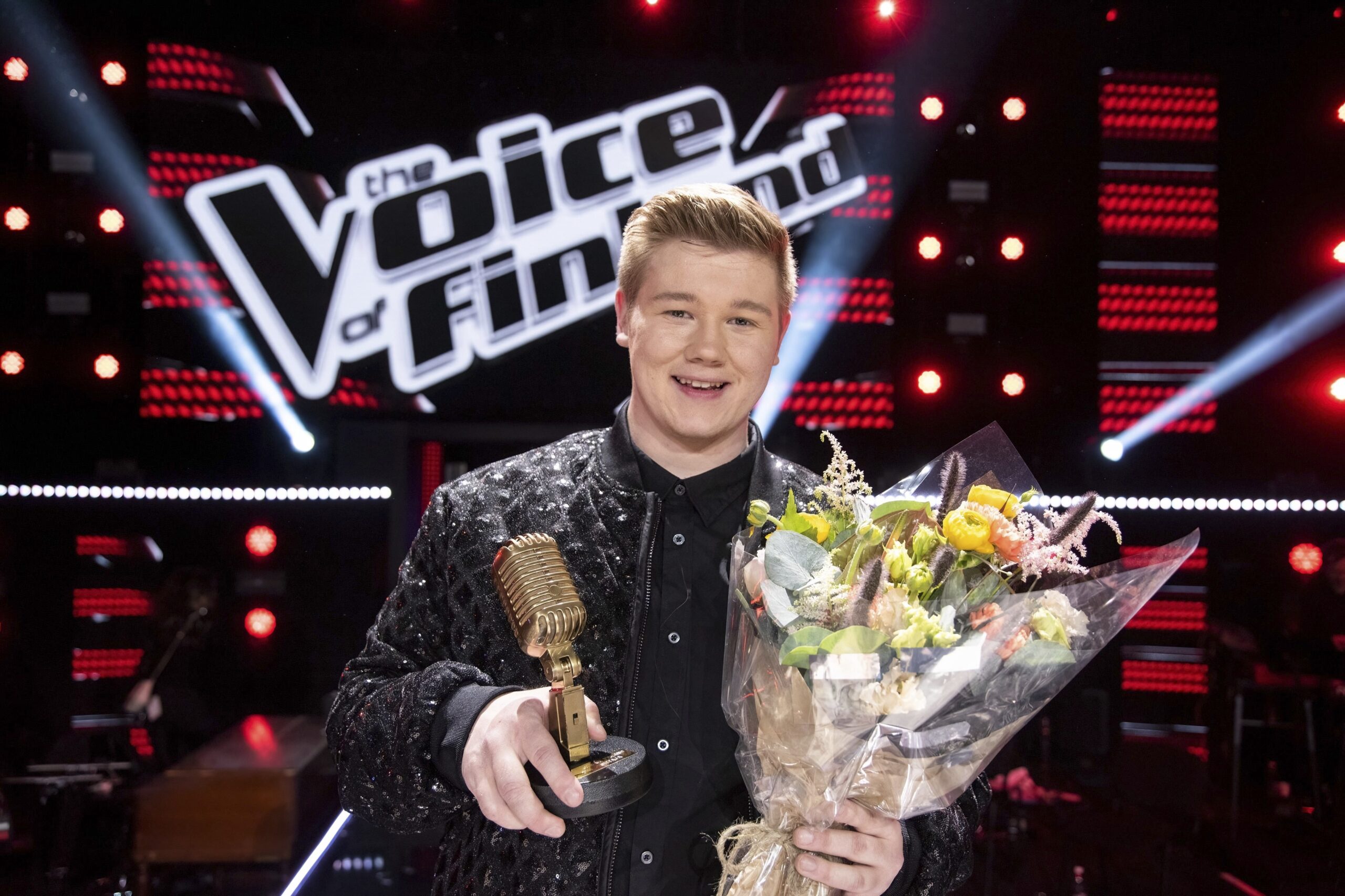 The Voice of Finland -kilpailun voittaja Onni Kivipelto pitelee voiton jälkeen palkintoaan sekä kukkia ja hymyilee kameralle.