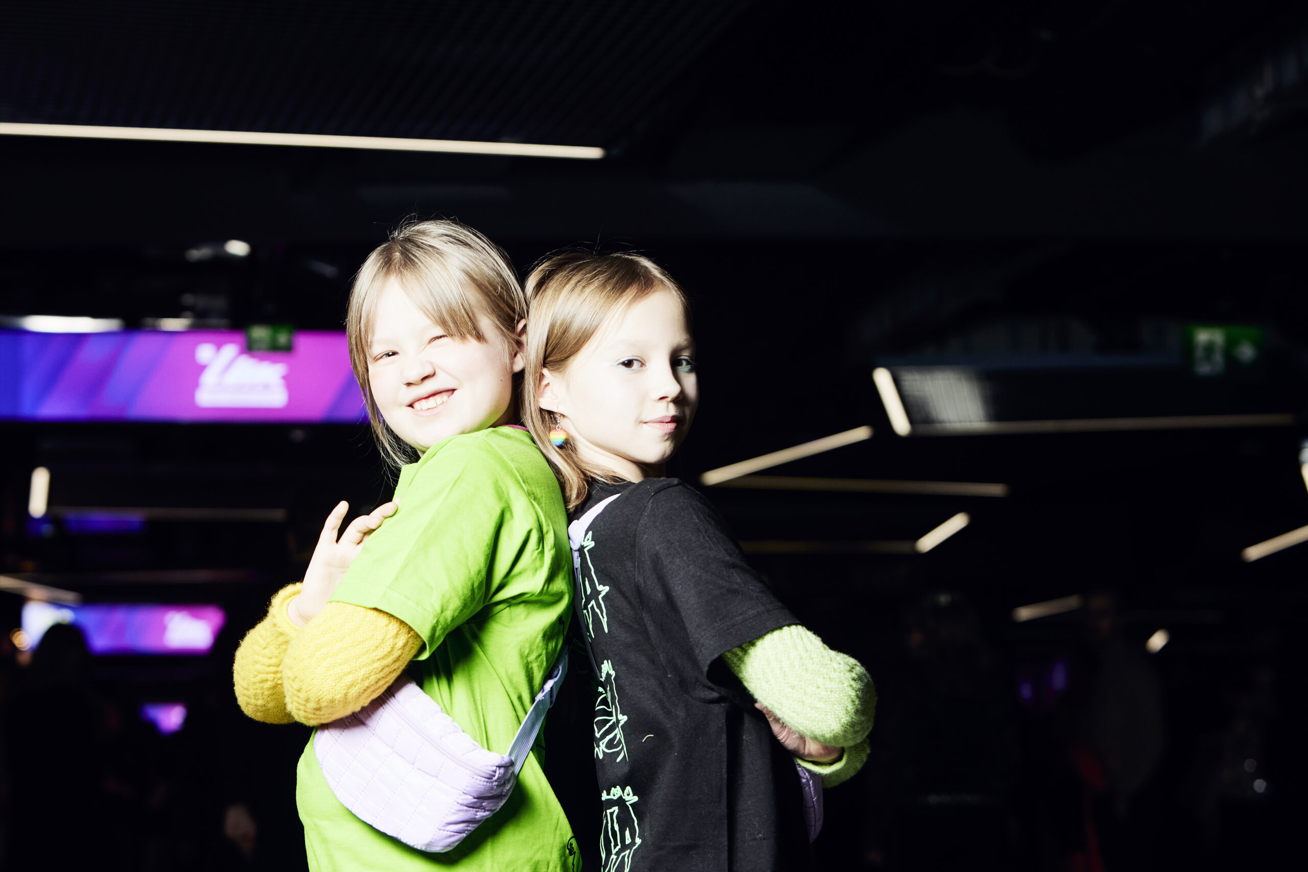 Vihreäpaitainen Klaara ja mustapaitainen Saara poseeraavat selät vastakkain Nokia Arenan käytävällä kameralle.