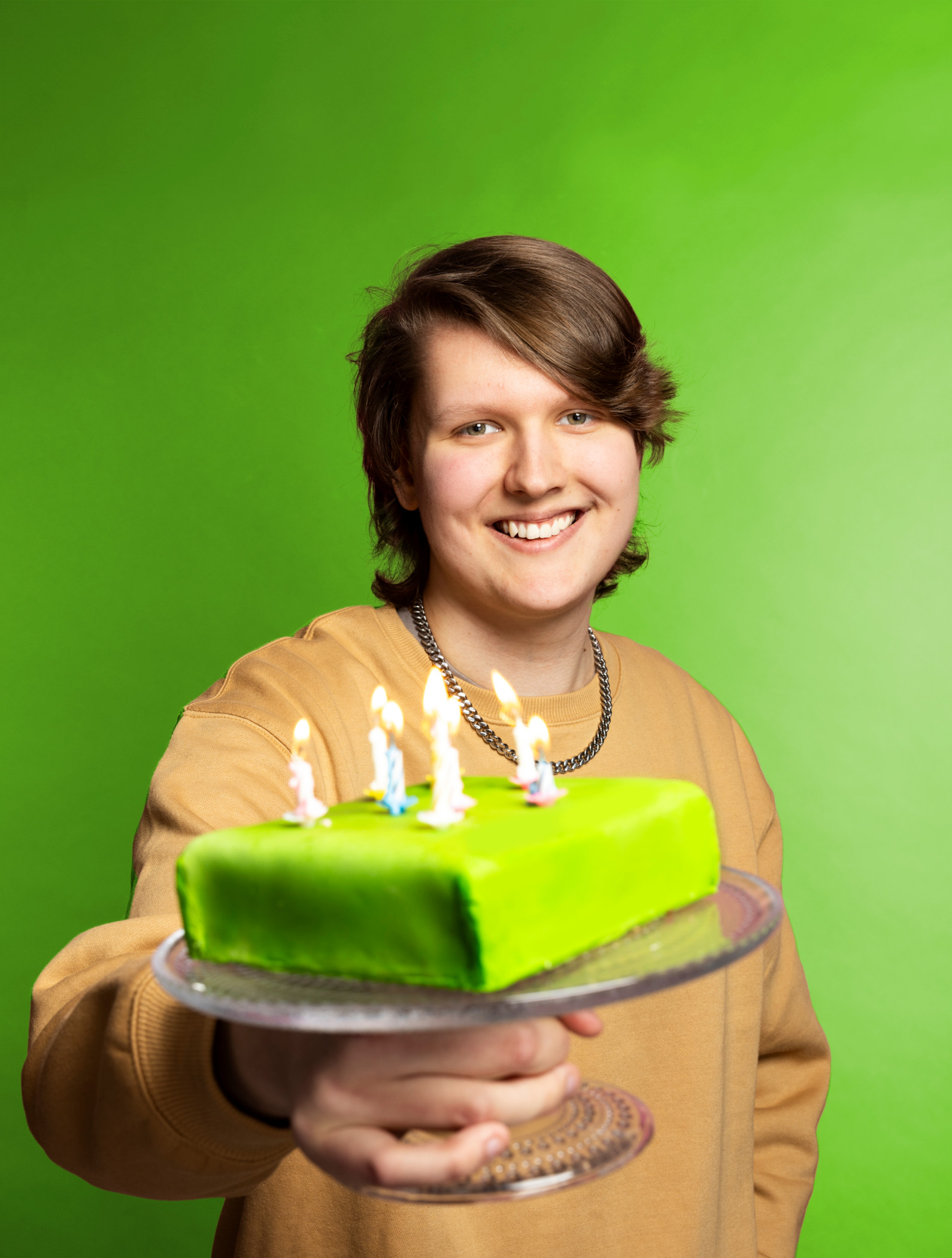 Kakkuh näyttää hymyillen kameralle vihreää kakkua, jossa palaa kahdeksan kynttilää.